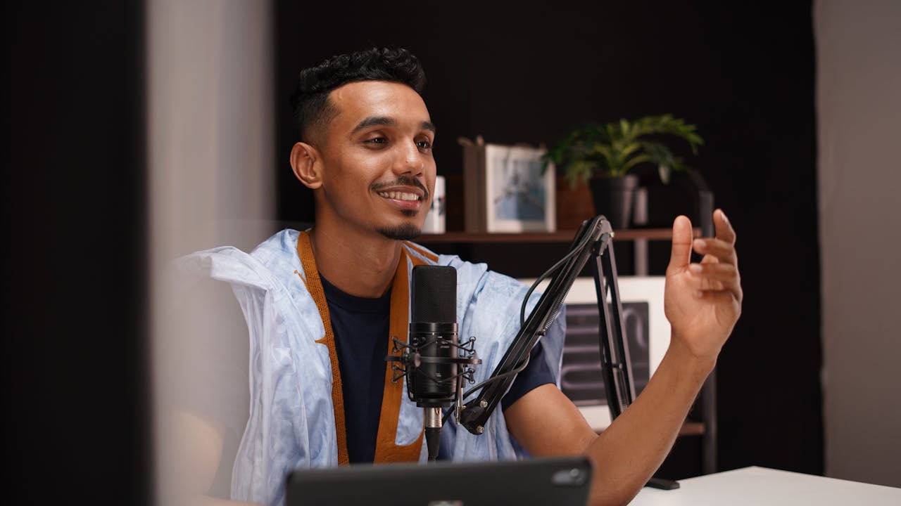 Smiling young man recording a podcast in a cozy home studio with professional microphone setup.
